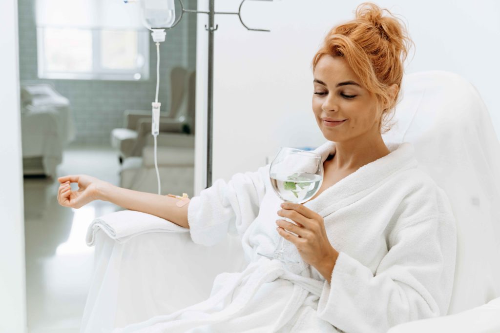 A Woman getting IV Therapy and holding glass with water | Rejuve Wellness in The Woodlands and Montgomery, TX