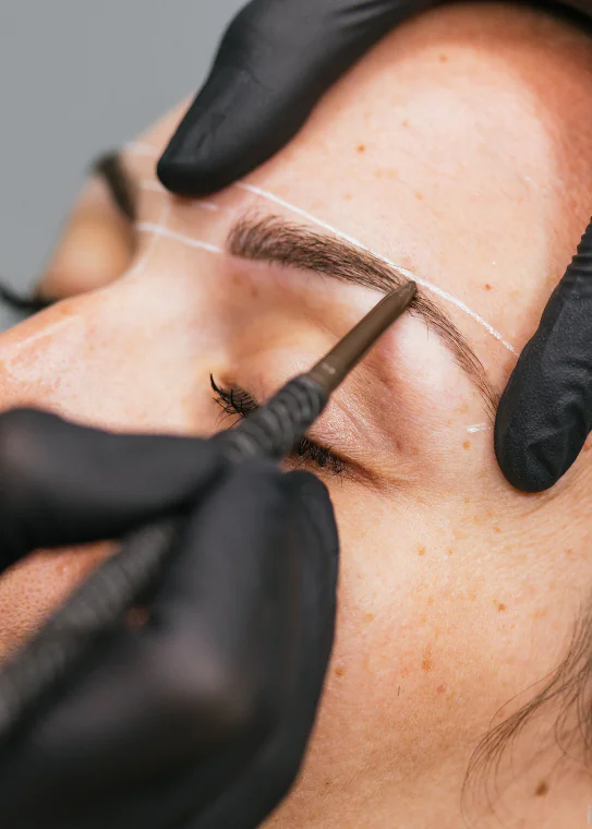 Brow artist mapping and shaping a client's eyebrow during a brow service